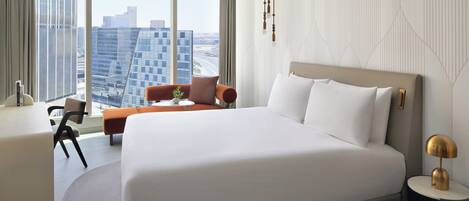 A modern hotel room with a large bed, a desk, and a view of the city skyline.