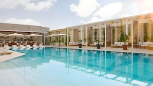 En swimmingpool med liggestole og parasoller, et barområde og indendørs planter.