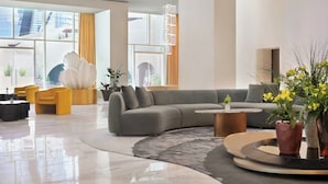 En moderne hotellobby med en buet sofa, gule stole, et rundt sofabord og potteplanter.
