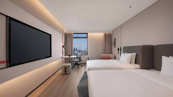 A modern hotel room with a large bed, a desk, a chair, and a large TV screen.