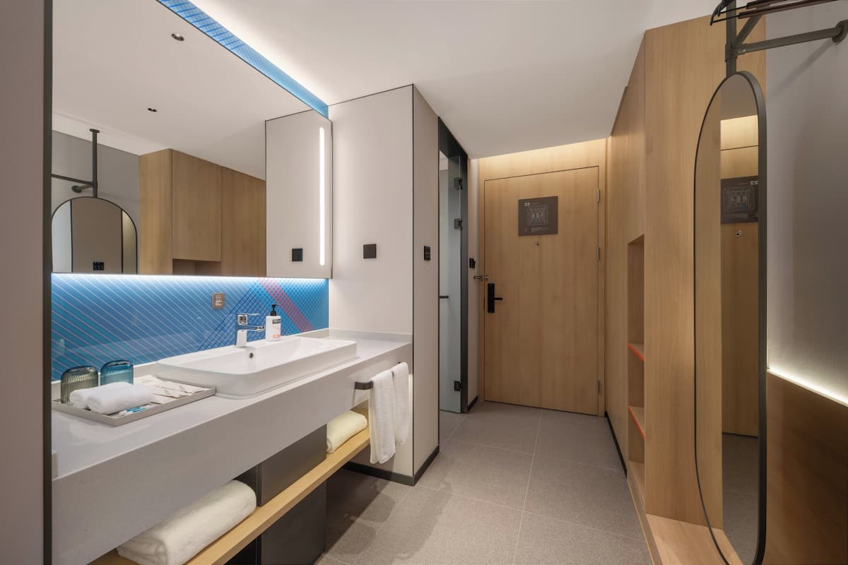 A modern bathroom with a large mirror, two sinks, a towel rack, and a shower area.