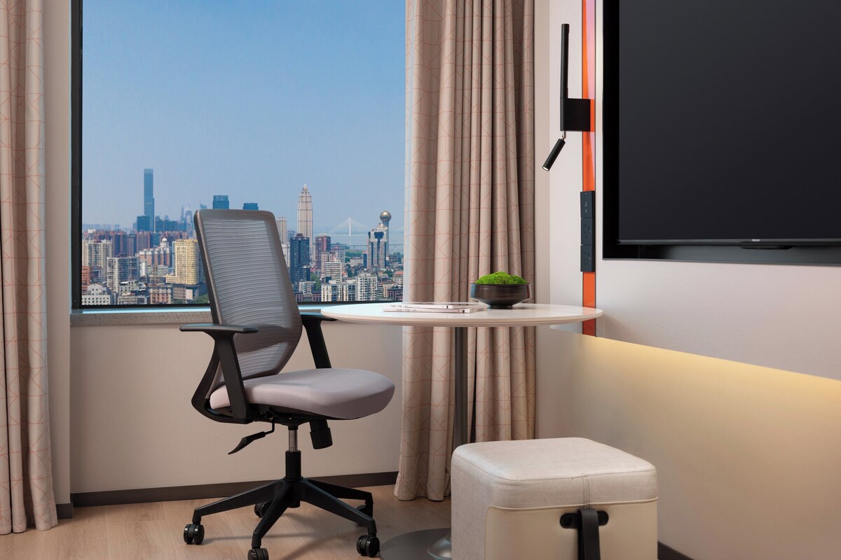 Een moderne kantoorruimte met uitzicht over de stad, een bureau met een plant en een grote televisie aan de muur.