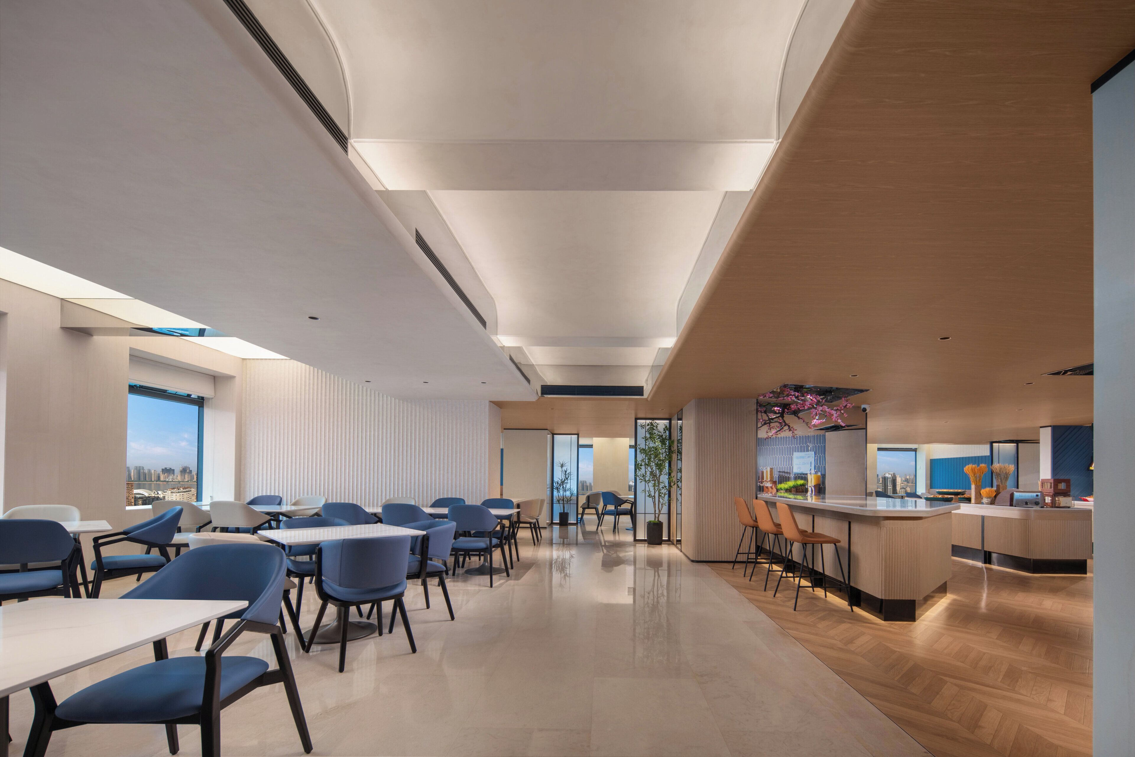A modern dining area with tables and chairs, a kitchen counter, and a view of the city.