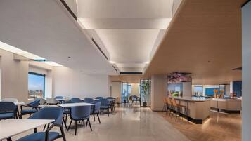 A modern dining area with tables and chairs, a kitchen counter, and a view of the city.