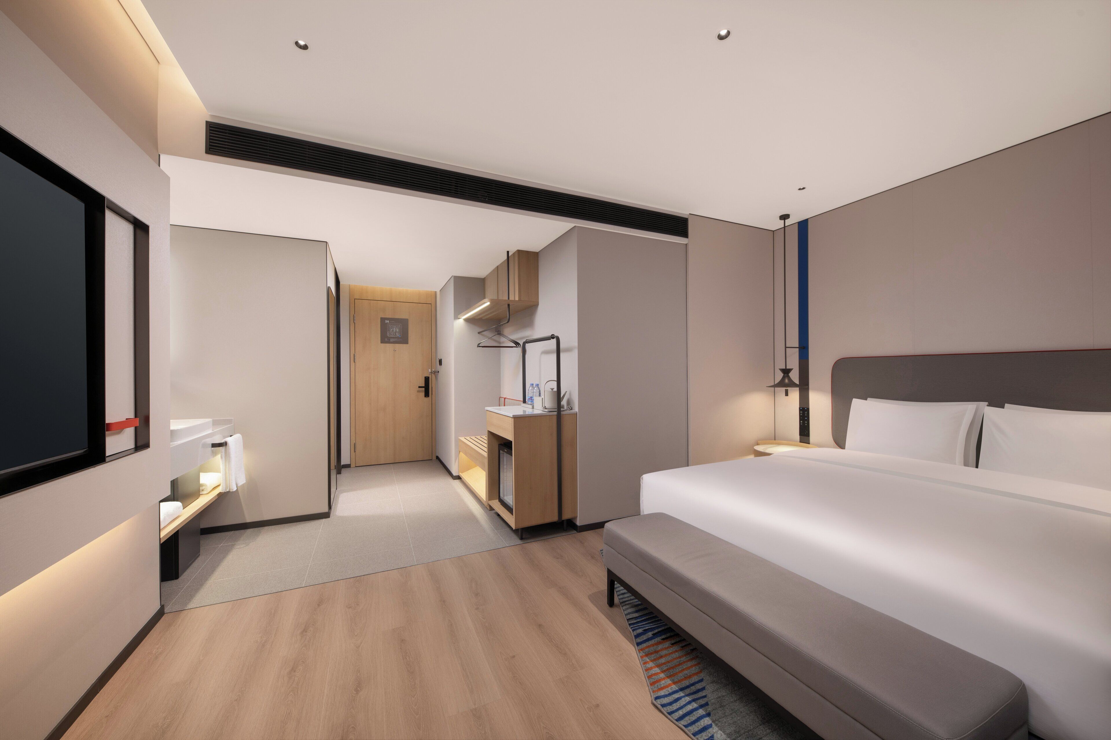 A modern hotel room with a large bed, a desk, a wardrobe, and a bathroom.
