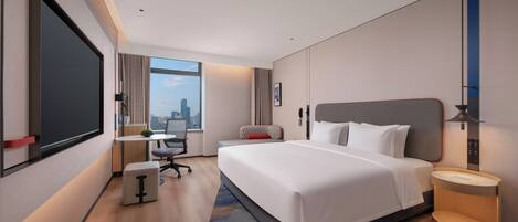 A modern hotel room with a large bed, a desk, a chair, and a view of the city.