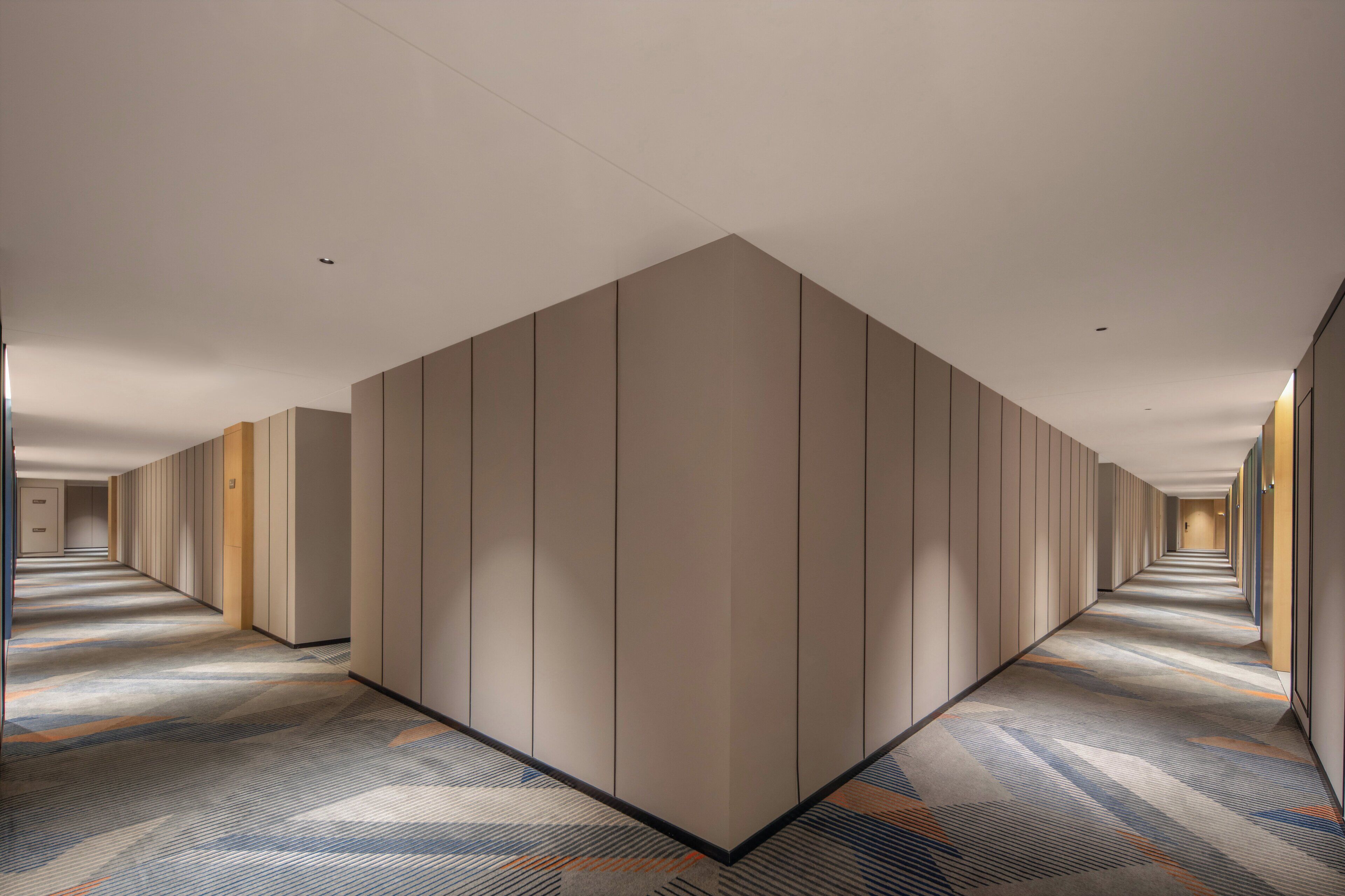 A long, narrow hotel corridor with a patterned carpet and neutral-toned walls.