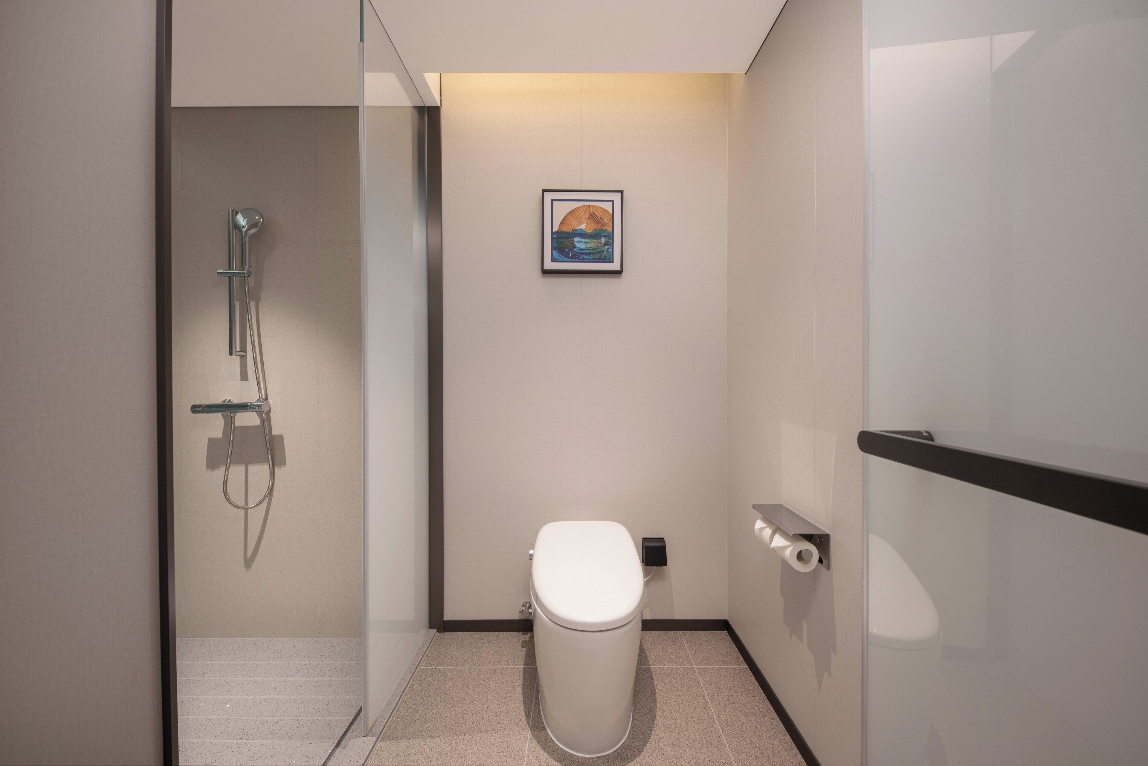 Un baño moderno con cabina de ducha de vidrio, inodoro y un cuadro enmarcado en la pared.