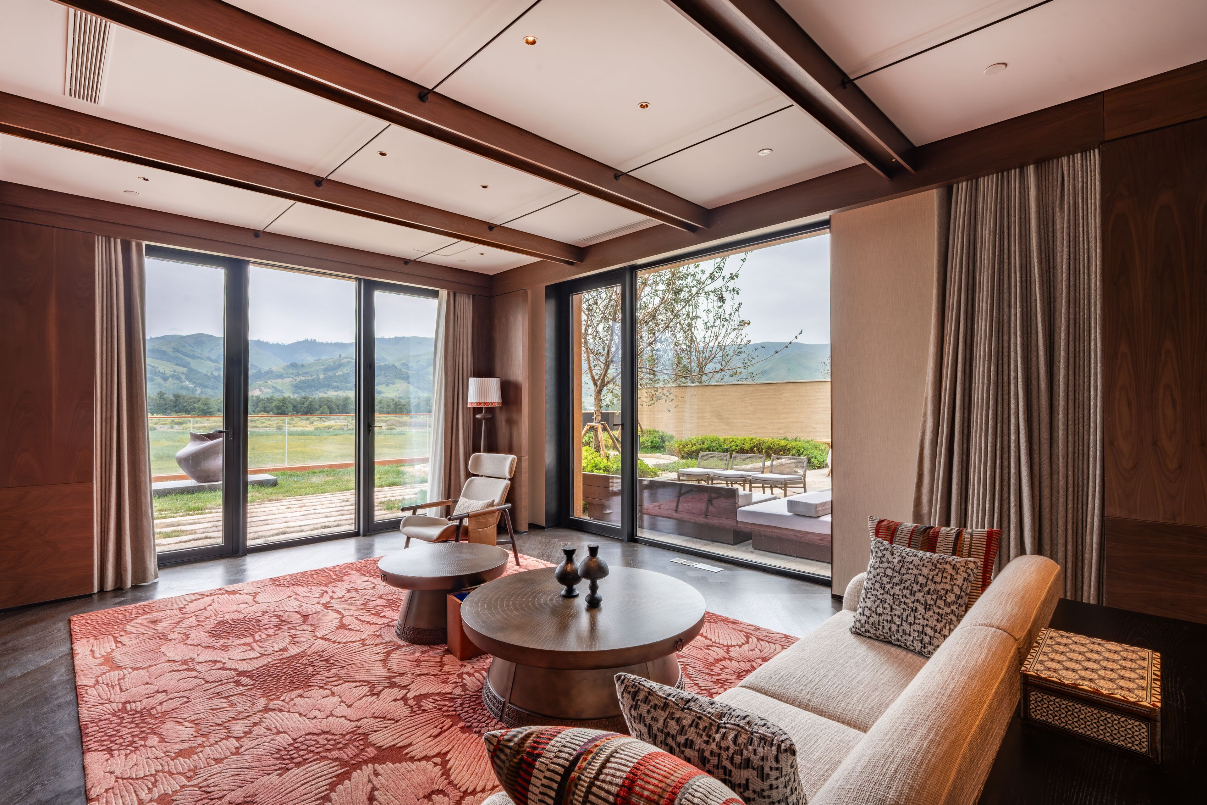 A modern hotel room with a large window, a sofa, a round table, and a patterned rug.