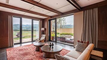 A modern hotel room with a large window, a sofa, a round table, and a patterned rug.
