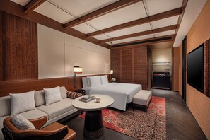 Una habitación de hotel moderna con cama, sofá, sillón, una mesita y televisor.
