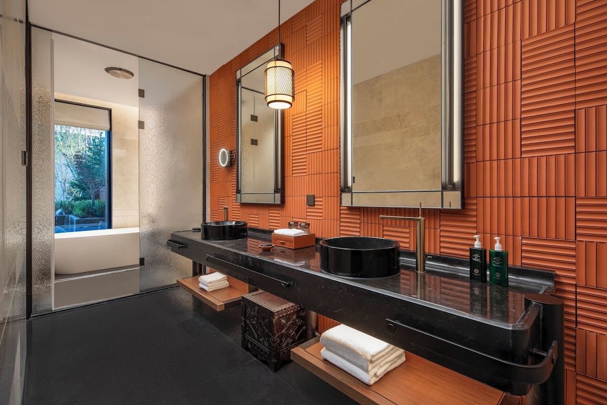 A modern bathroom with a black countertop, wooden panel wall, and a large mirror.
