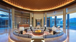 A spacious lobby with a circular seating area, large windows offering views of the outdoors, and a high ceiling with a geometric pattern. - Hotel Indigo Nalati by IHG (Xinyuan)