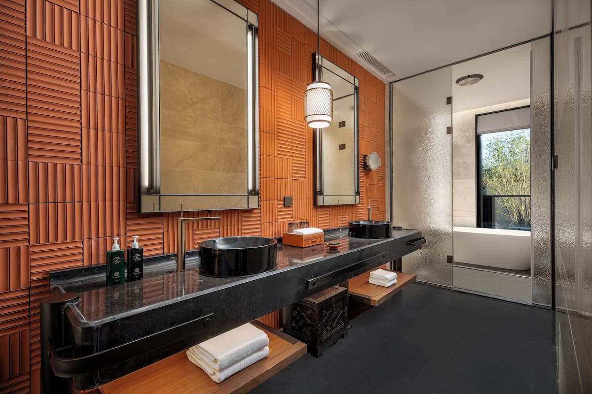 A modern bathroom with a black countertop, wooden panel wall, and a large mirror.