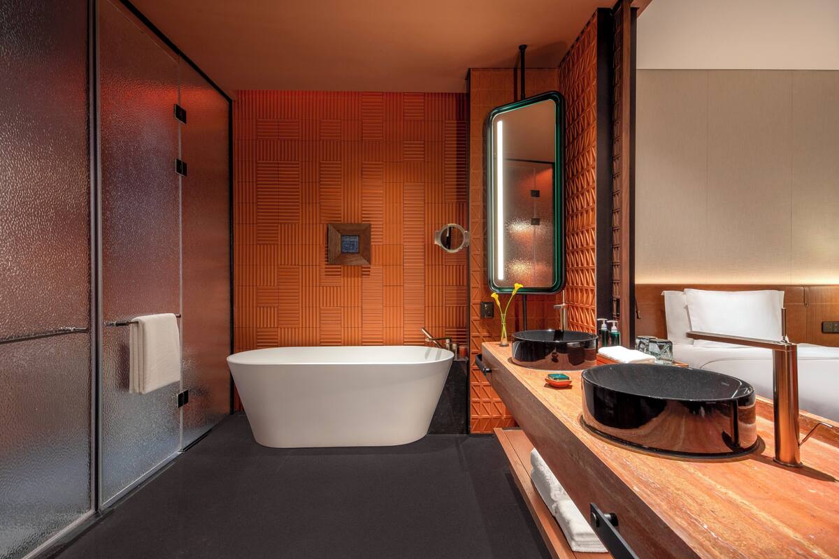 Un baño moderno con una bañera independiente, un espejo grande y un tocador de madera con lavamanos negro.