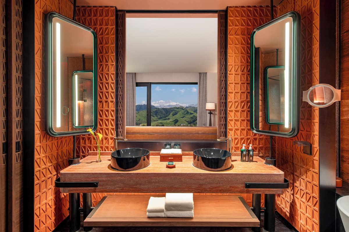 A bathroom with a wooden vanity, two black bowls, a window with a mountain view, and a mirror with a light strip.
