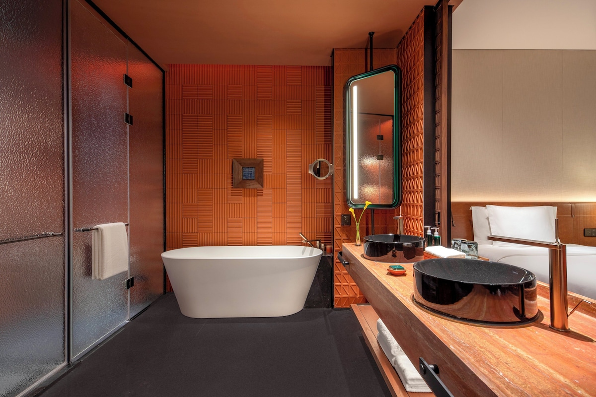 Un baño moderno con una bañera independiente, un espejo grande y un tocador de madera con lavamanos negro.