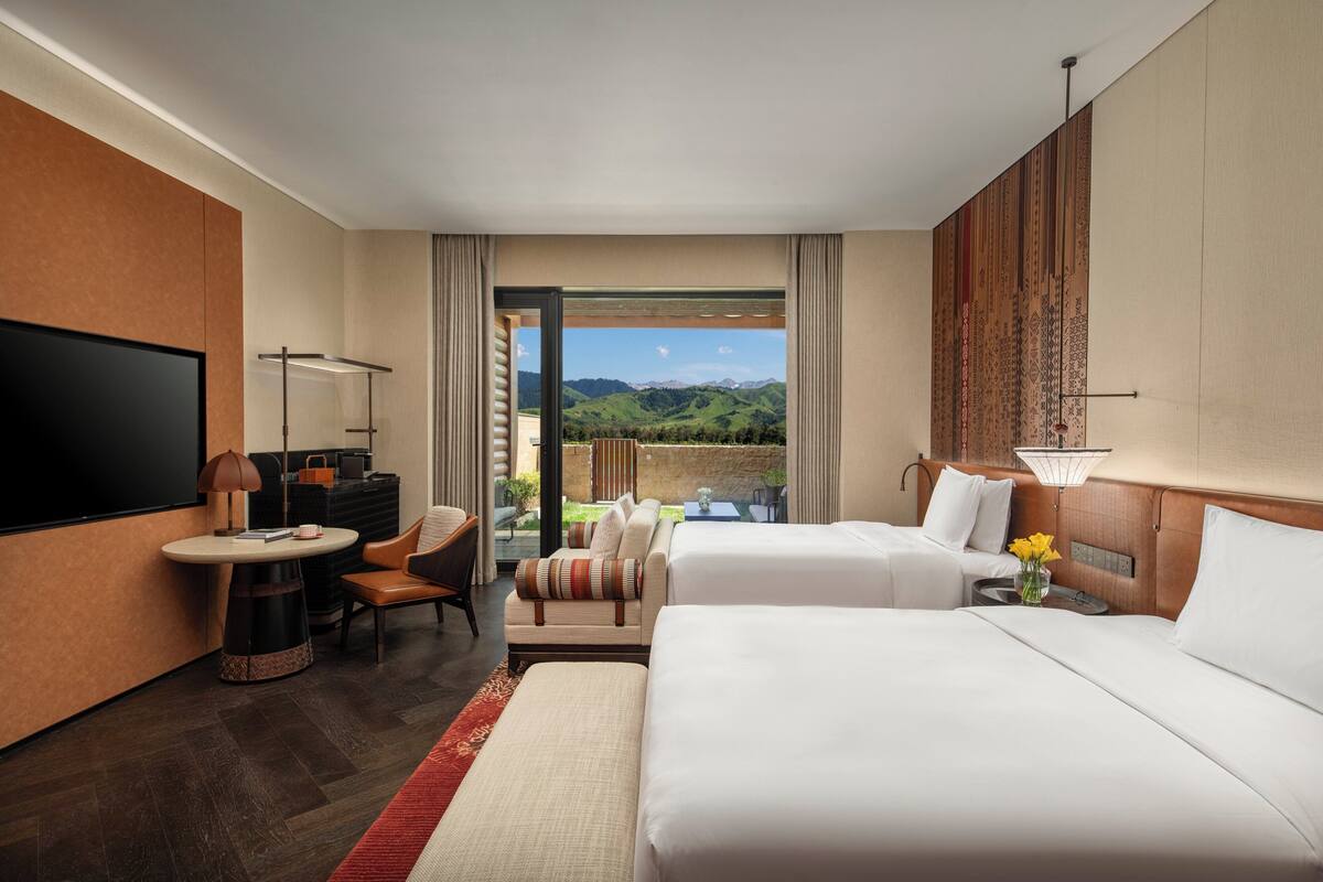 Habitación de hotel con televisor grande, sofá, cama y vistas a las montañas.