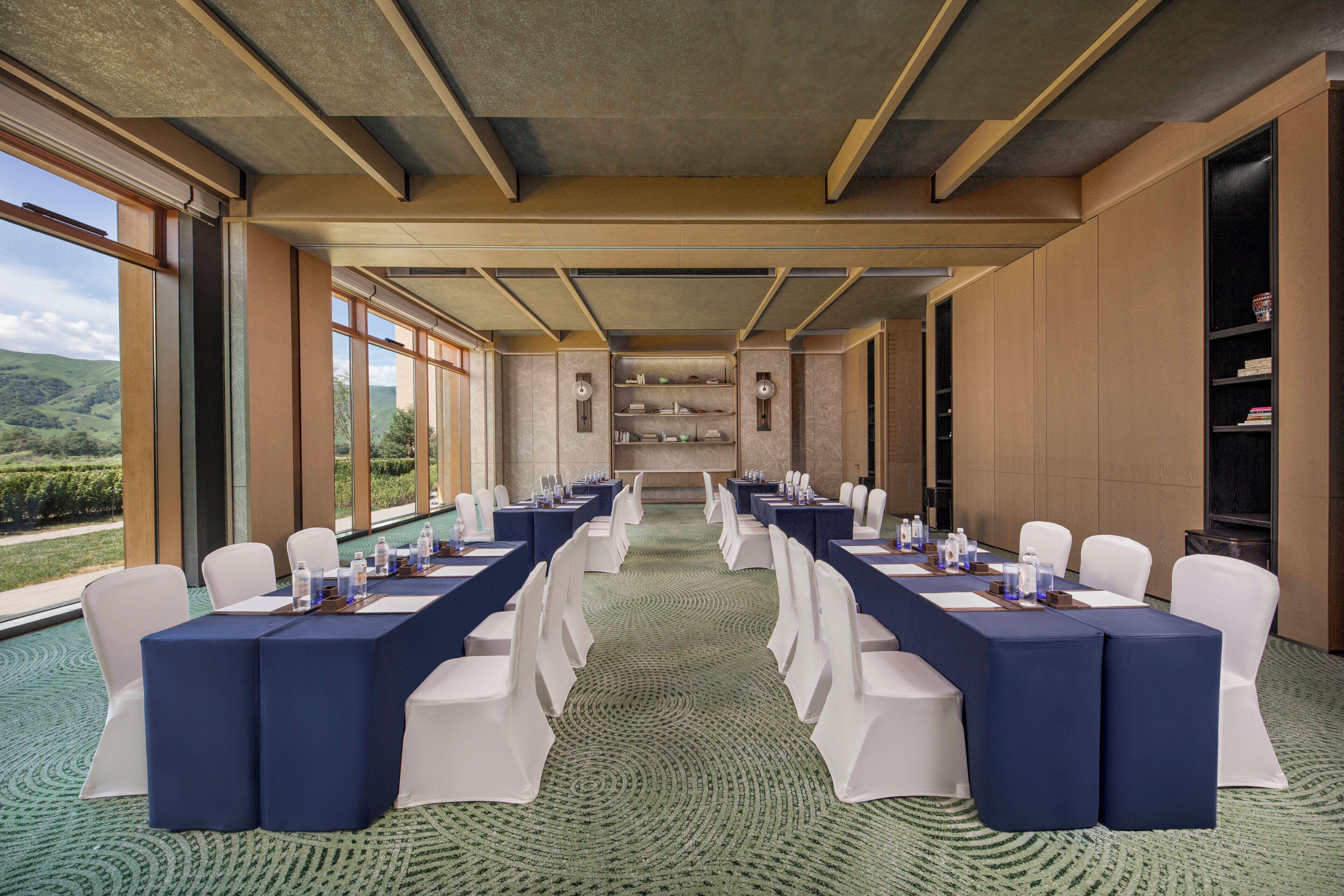Une salle de conférence avec une longue table, des chaises blanches et une vue sur l’extérieur.