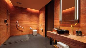 A modern bathroom with a wooden wall, a large mirror, a black sink, and a towel rack.