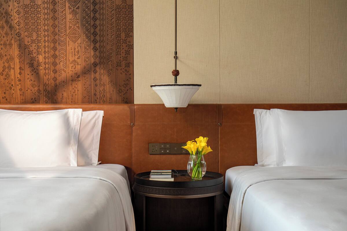Habitación de hotel con dos camas, una mesita de noche con un florero y una pared con diseño decorativo.