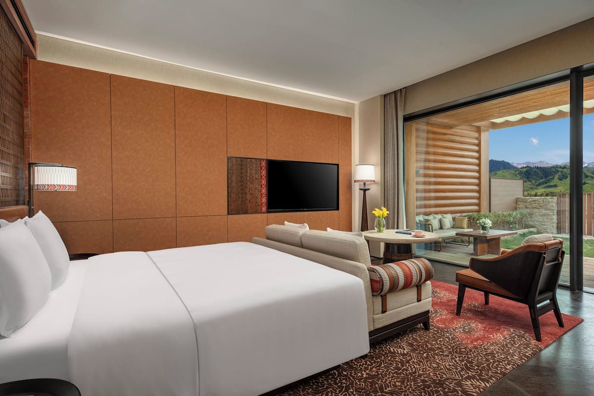 A hotel room with a large bed, a sofa, a TV, and a balcony with a table and chairs.