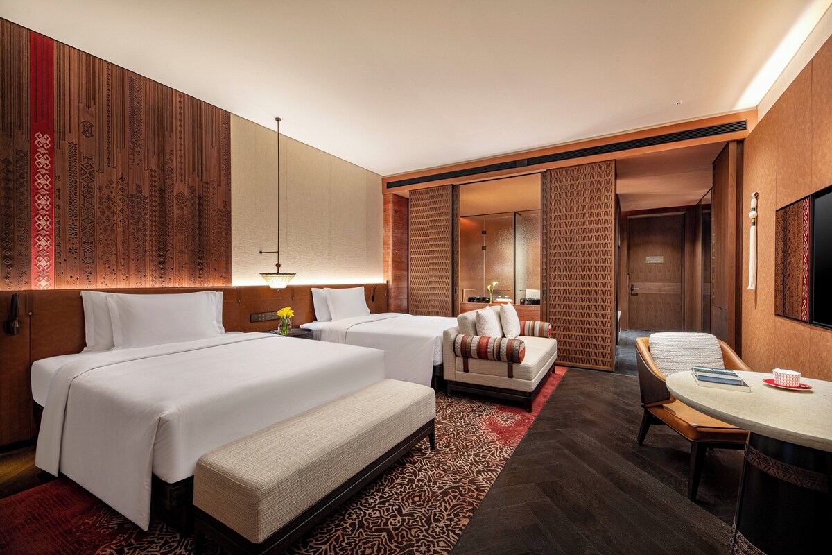 A hotel room with two beds, a sofa, a dining table, and a TV.