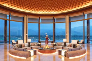 Un vestíbulo espacioso con una chimenea central, amplias ventanas que ofrecen vistas a la montaña y un techo alto con un diseño geométrico.