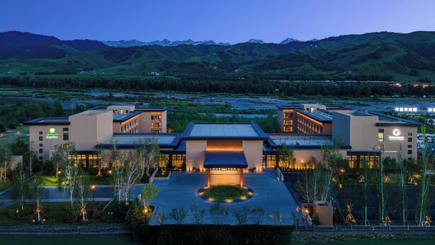 A modern hotel with a central courtyard, surrounded by landscaped areas and a view of mountains. - Holiday Inn Express Nalati by IHG (Xinyuan)