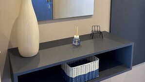 A modern bathroom vanity with a large mirror, a white vase, a small blue container, and a wicker basket. - Blue Apartment - Verona & Lake (San Vito Al Mantico)
