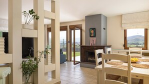 Een ruime woonkamer met een open haard, eettafel en uitzicht op de omgeving.