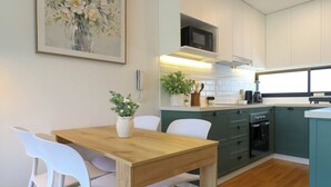A modern kitchen with white chairs, a wooden table, green cabinets, and a microwave. - Pendragon by Wynwood House (Lima)