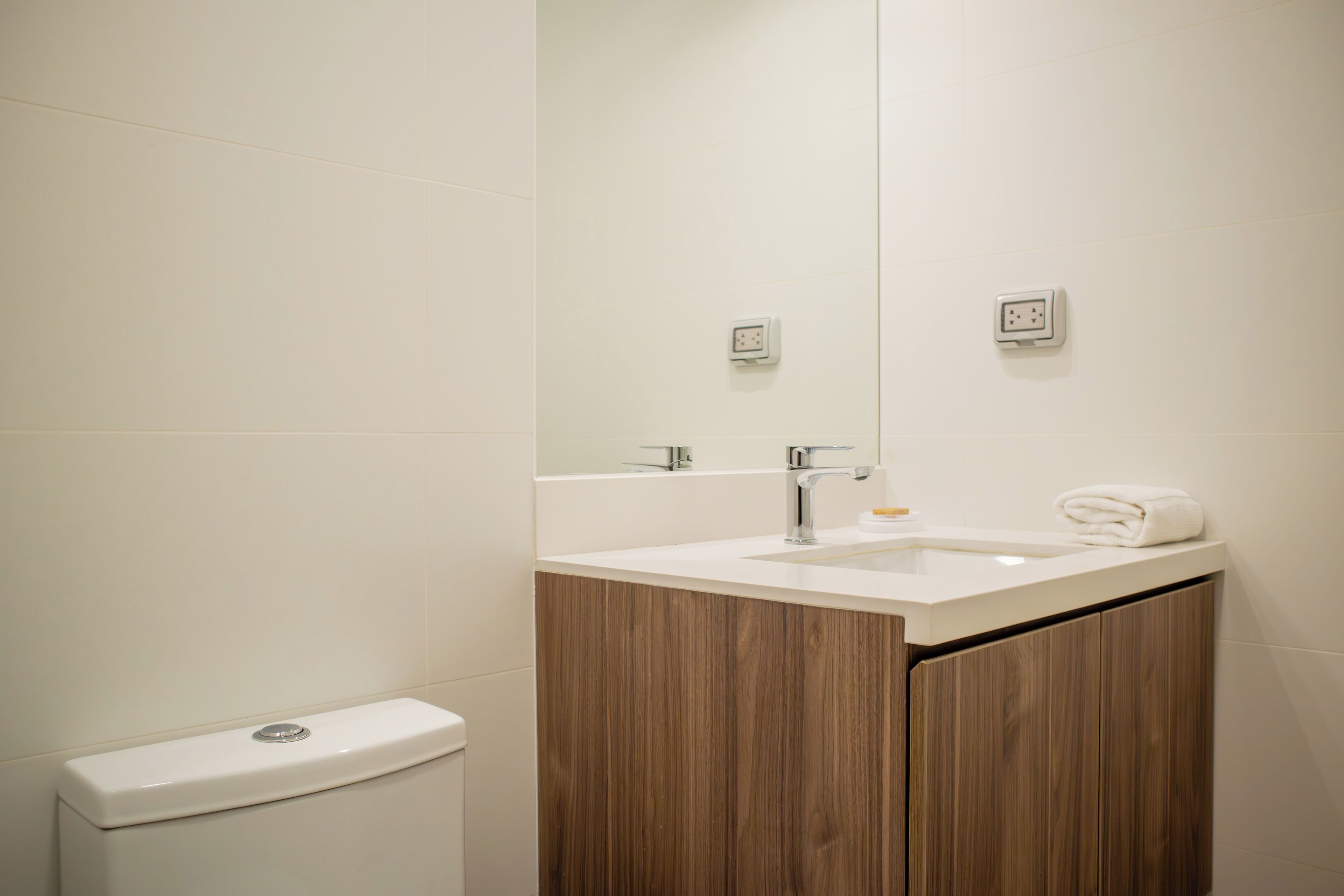 Ein modernes Badezimmer mit einem weißen Waschbecken, einer Holz-Waschkommode und einem Spiegel.