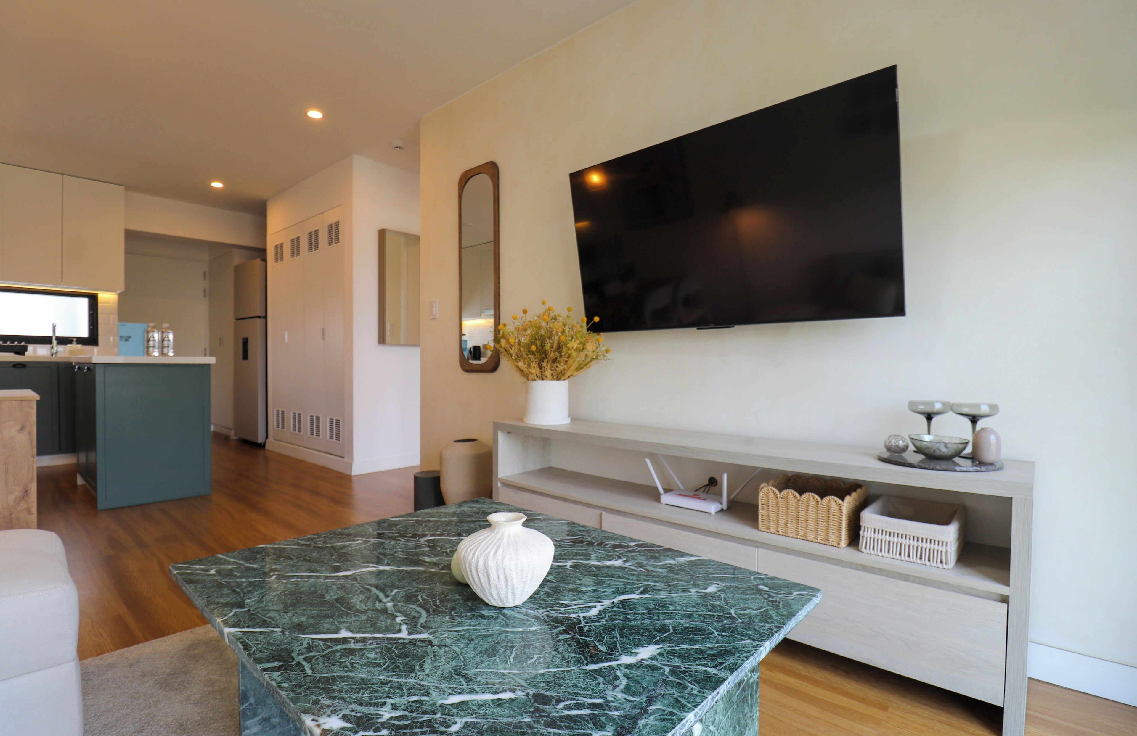 Uma sala de estar moderna com uma mesa de centro de mármore, uma TV de tela plana na parede e um console minimalista com objetos decorativos.