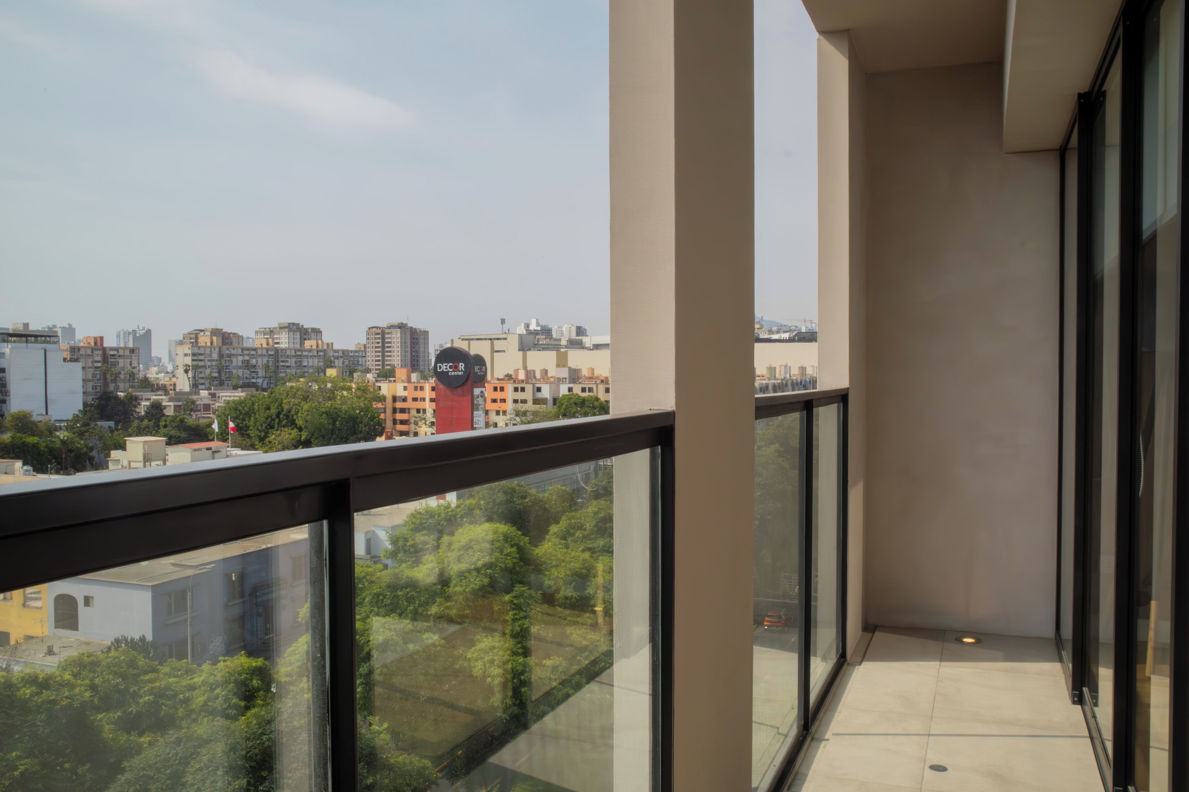 A balcony with a city view, glass railings, and a tiled floor.