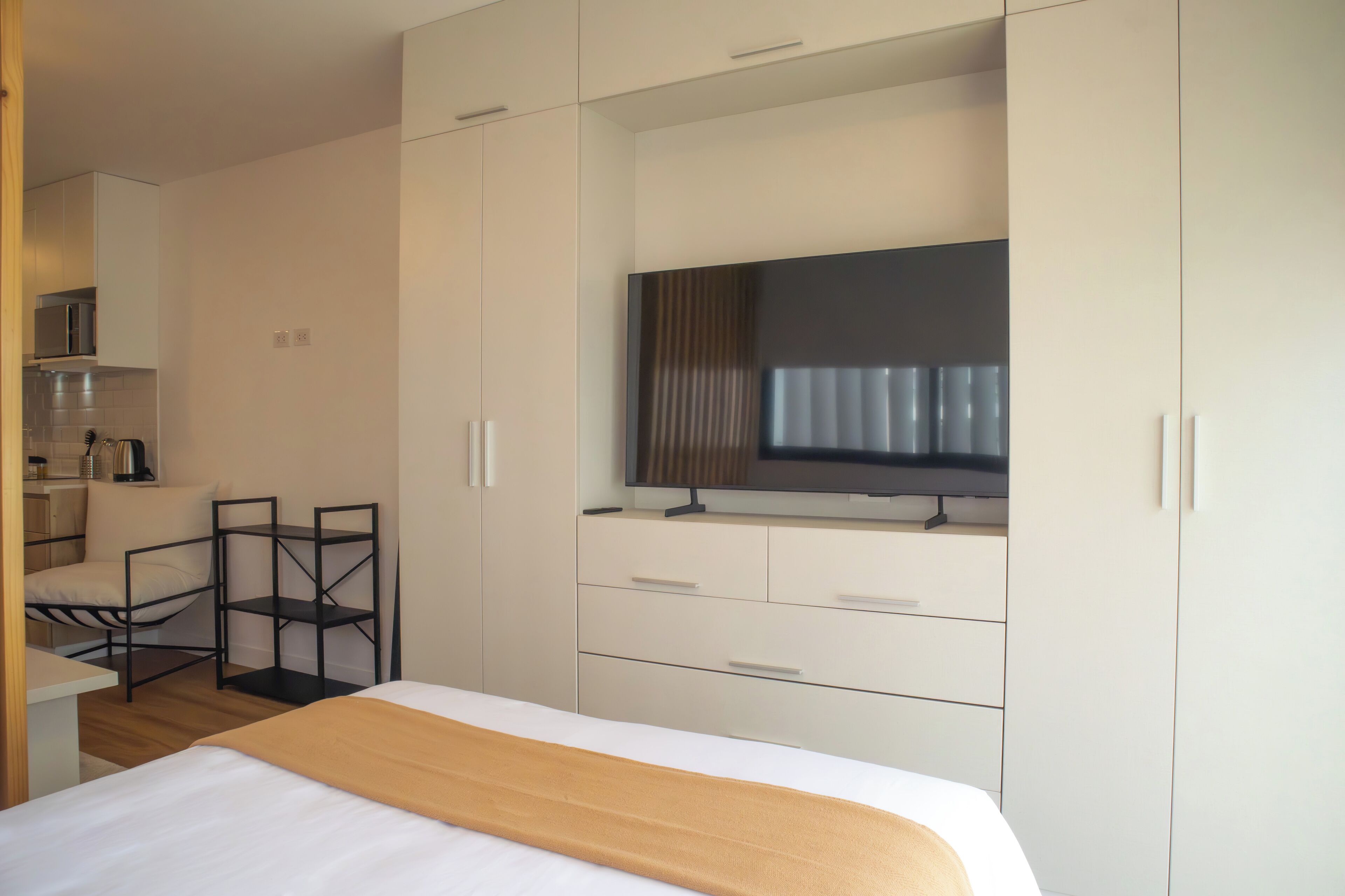 Una habitación de hotel moderna con una cama, un televisor montado en un mueble, un escritorio y una silla.
