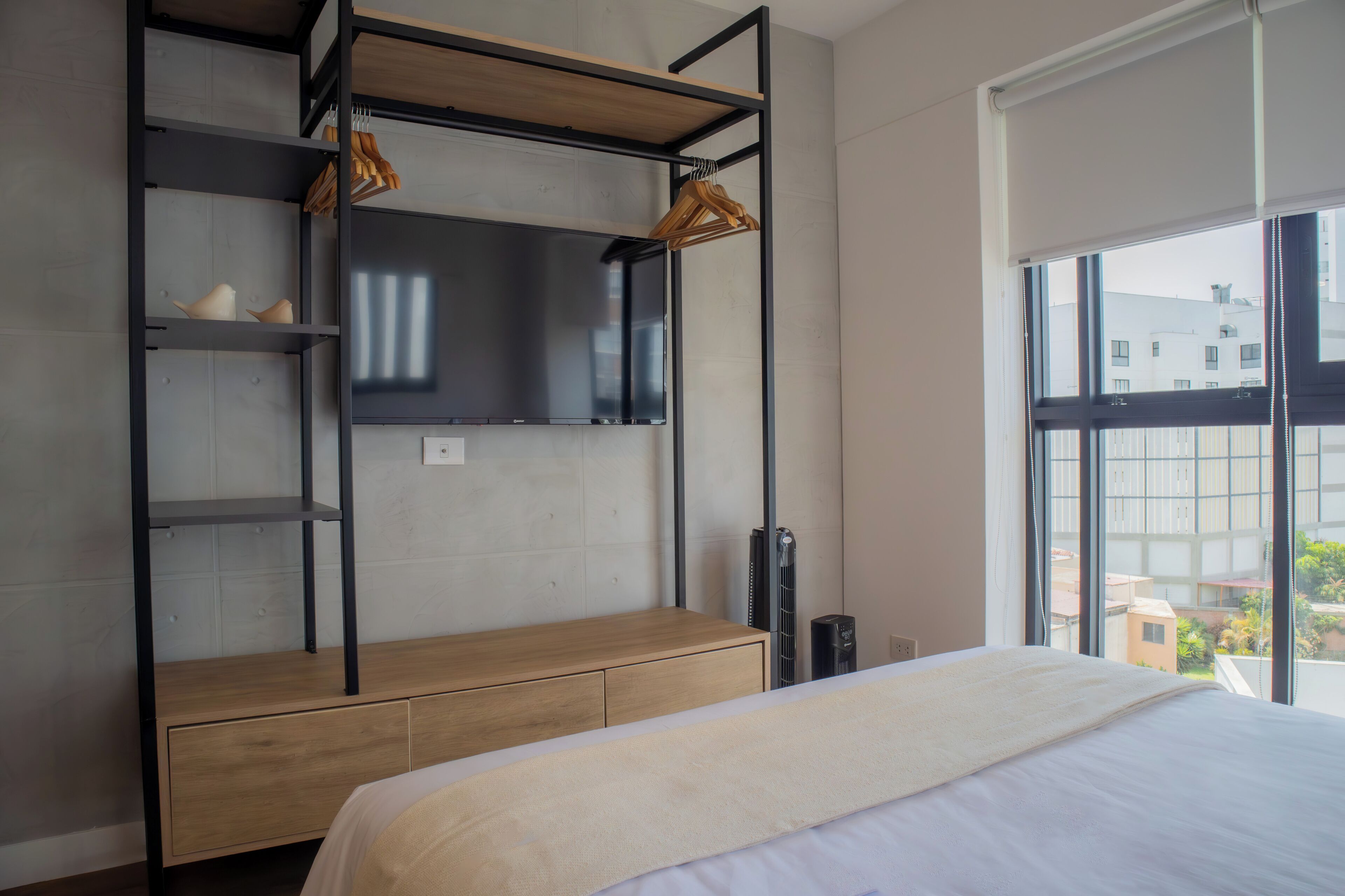 A bedroom with a bunk bed, wooden storage unit, and a large window with a city view.