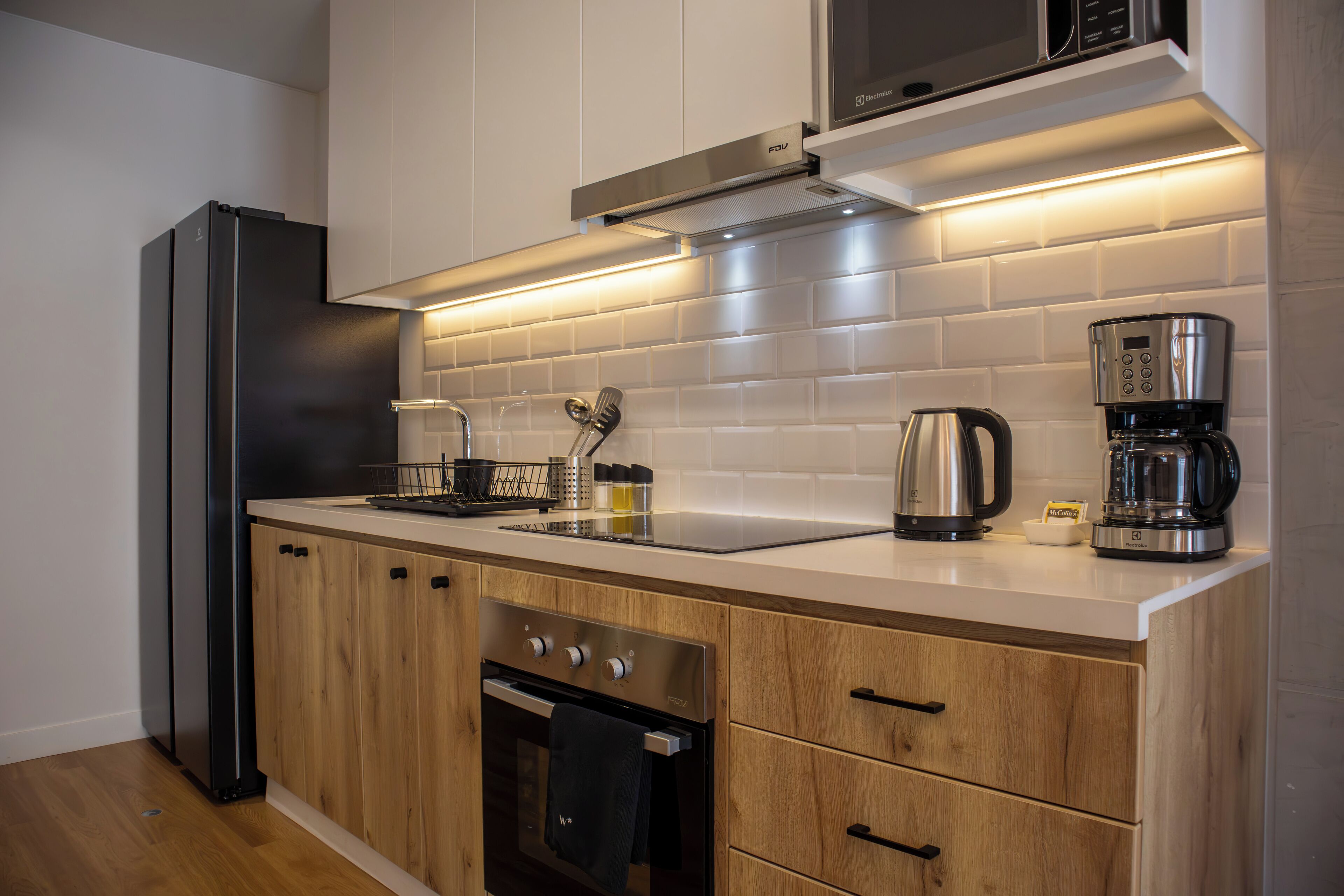 A modern kitchen with a built-in oven, a coffee maker, and a kettle on the countertop.