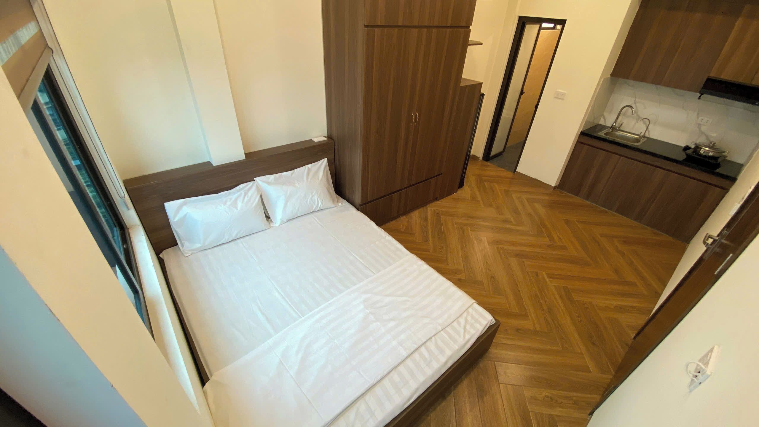A bedroom with a bed, wooden wardrobe, and a kitchenette.