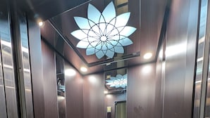 Interior d'un ascensor amb parets de fusta, un terra de marbre i una làmpada al sostre.