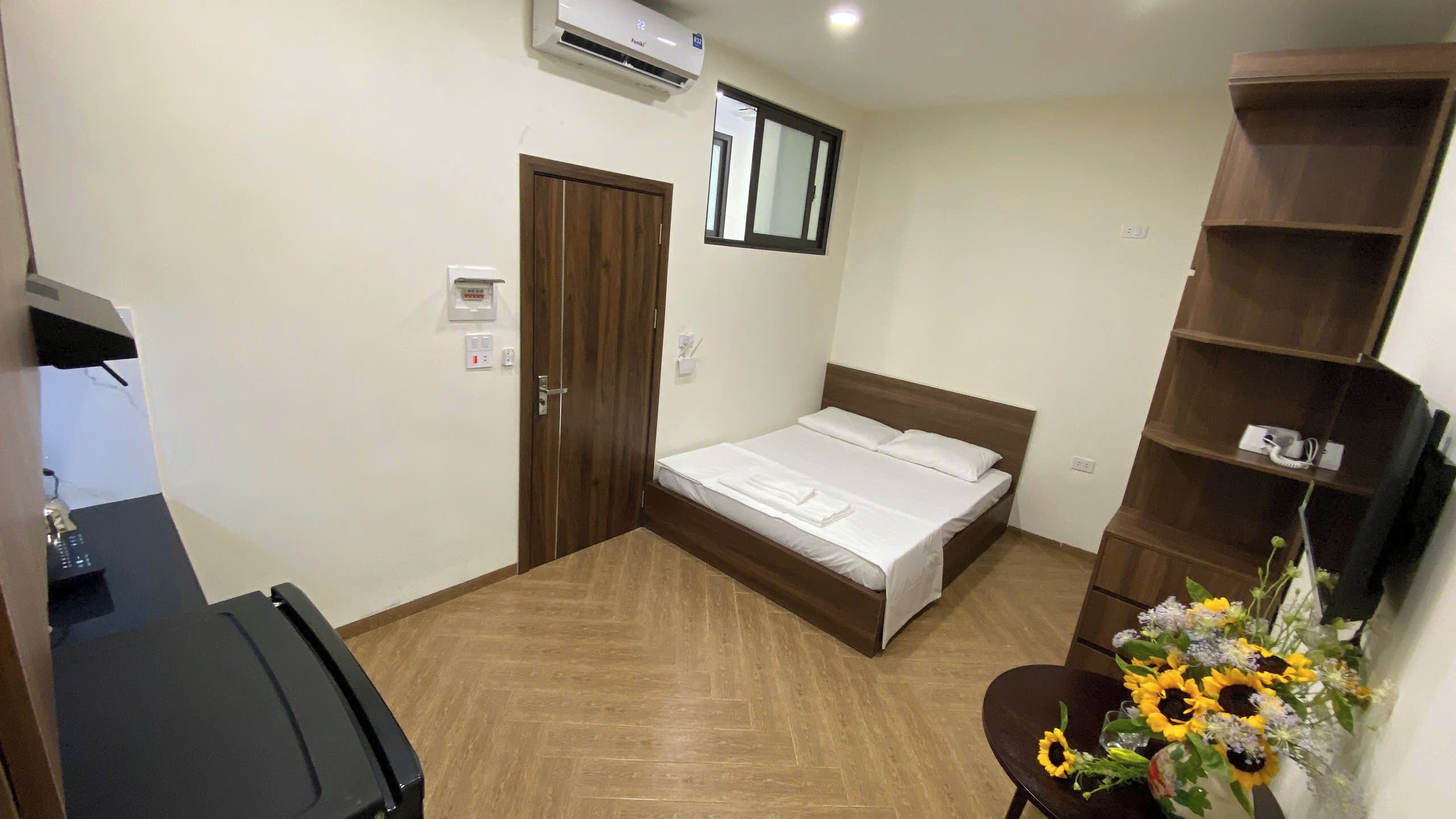 A hotel room with a bed, a desk, a chair, a shelf, and a wall-mounted air conditioner.