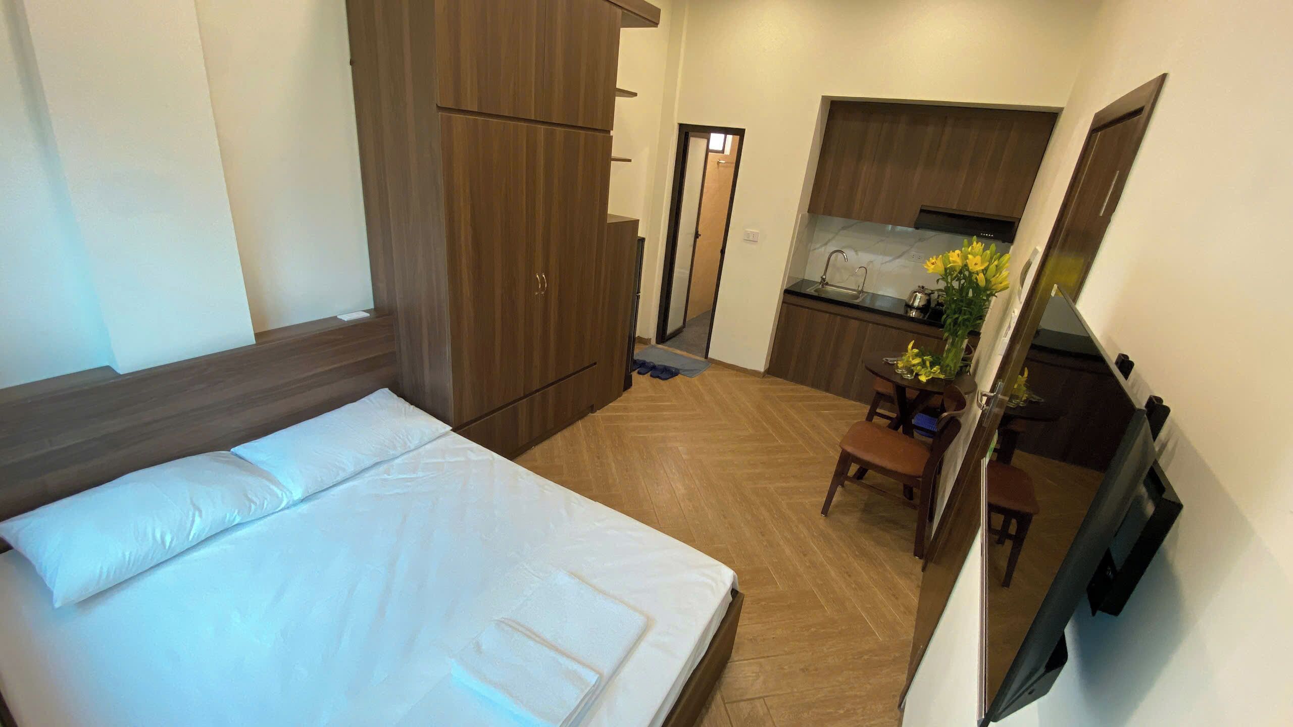 A hotel room with a bed, a wooden wardrobe, a small kitchen area with a sink and a dining table.