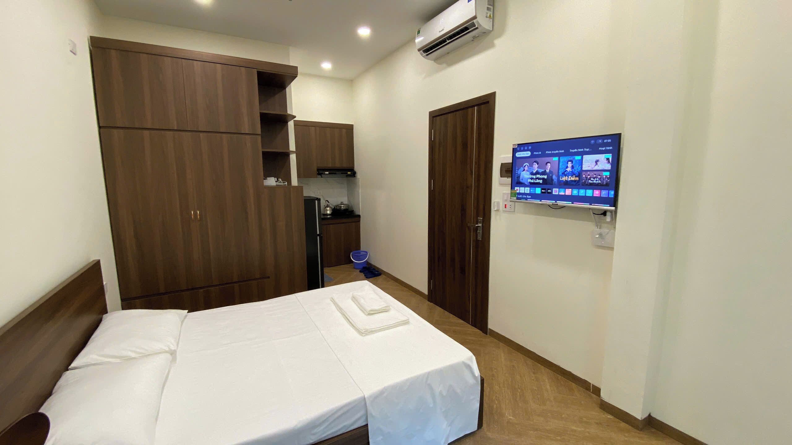 A hotel room with a bed, a TV mounted on the wall, a wardrobe, and a small kitchenette.