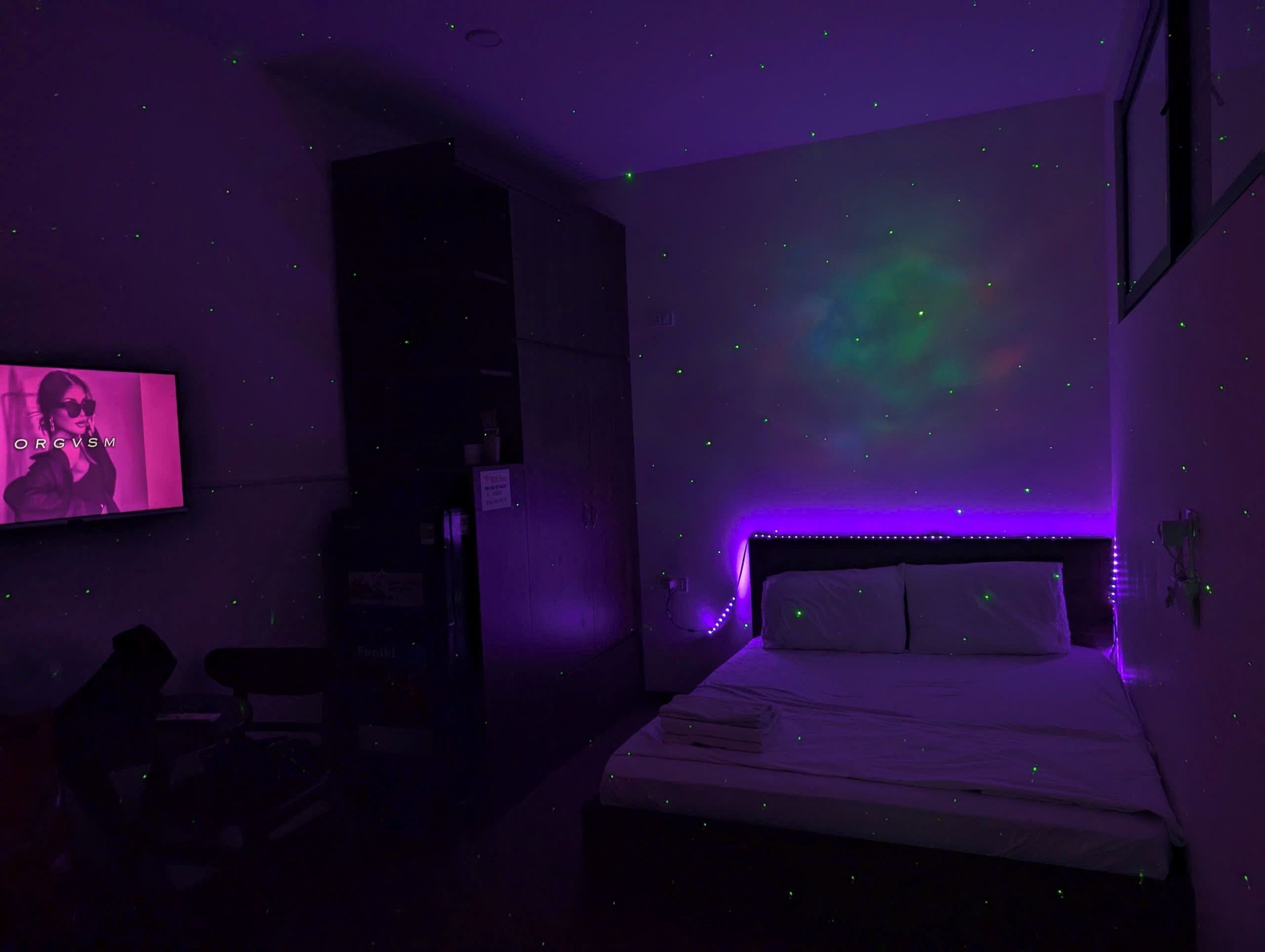 A room with a bed, a TV, and a wall projection.