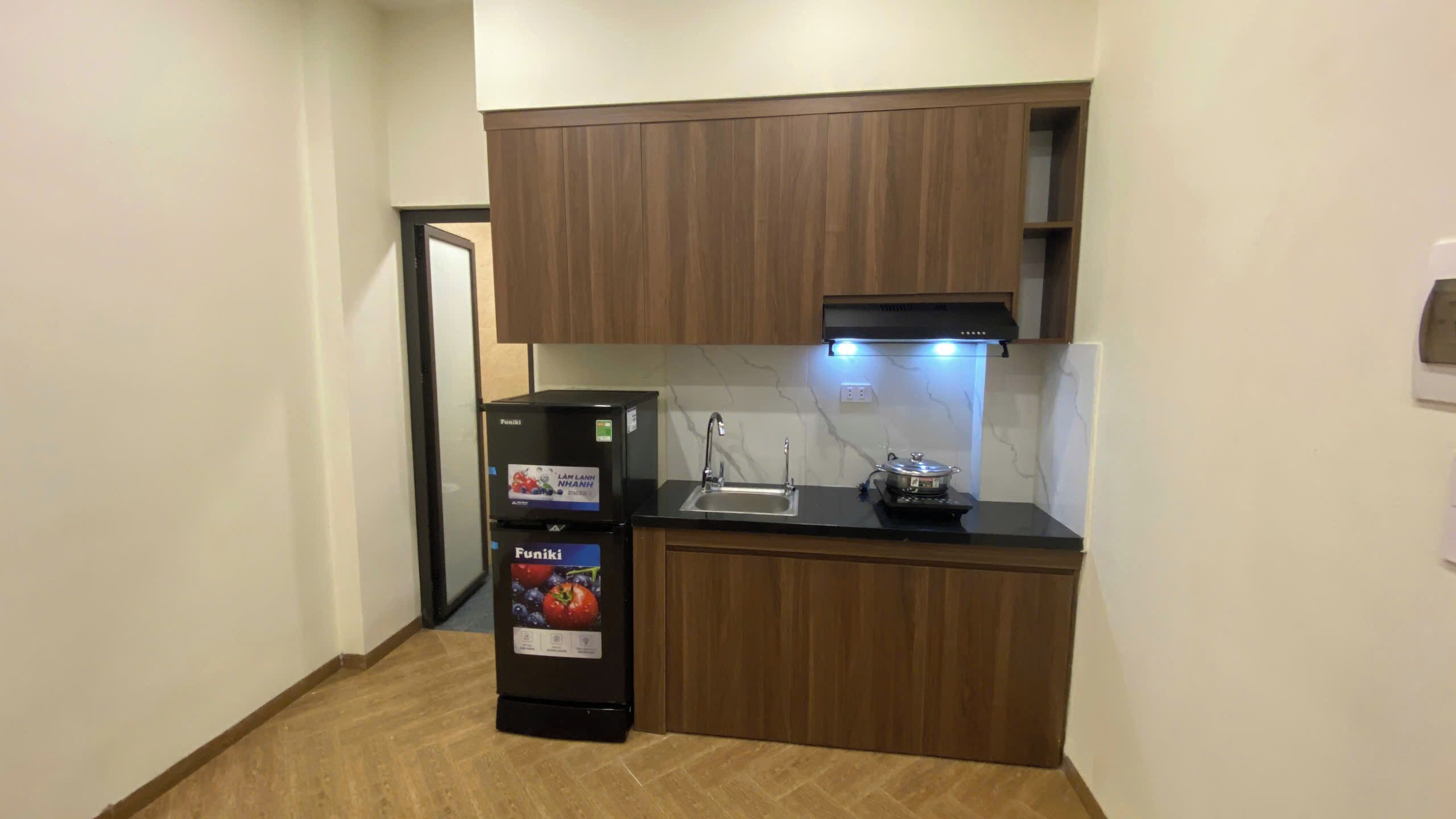 Une cuisine de taille réduite, avec des meubles de rangement en bois, un réfrigérateur noir, un évier et une cuisinière.