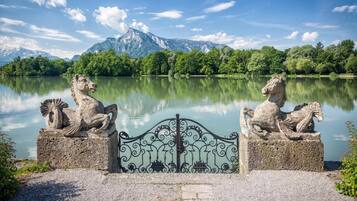 Eine Steinstatue eines Löwen auf einem Sockel, neben einem See mit Bergen im Hintergrund.