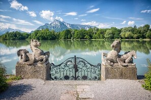 A stone statue of a lion on a pedestal by a lake with mountains in the background. - Schloss Leopoldskron Meierhof (Salzburg)
