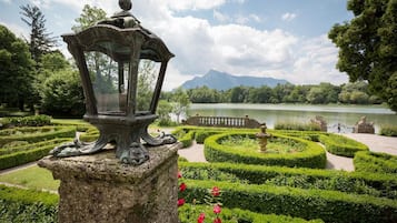 Ein Garten mit einer Steinhlaterne, geschnittenen Hecken und Blick auf einen See.
