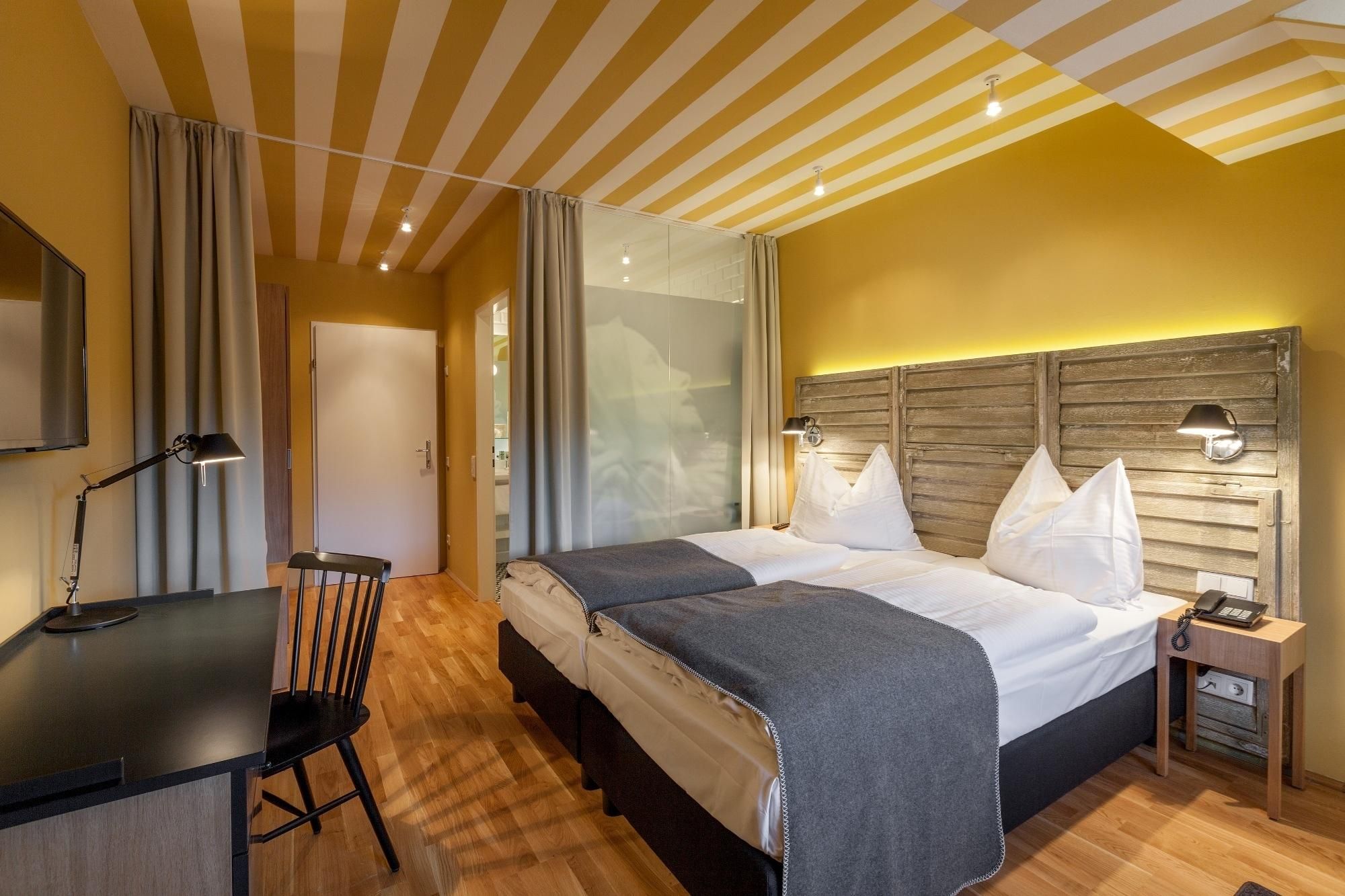 A hotel room with a bed, bedside table, lamp, and a desk with a chair.