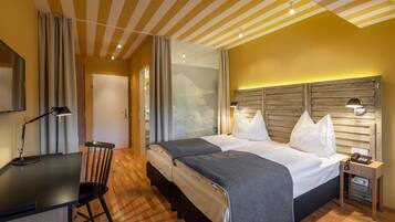 A hotel room with a bed, bedside table, lamp, and a desk with a chair.